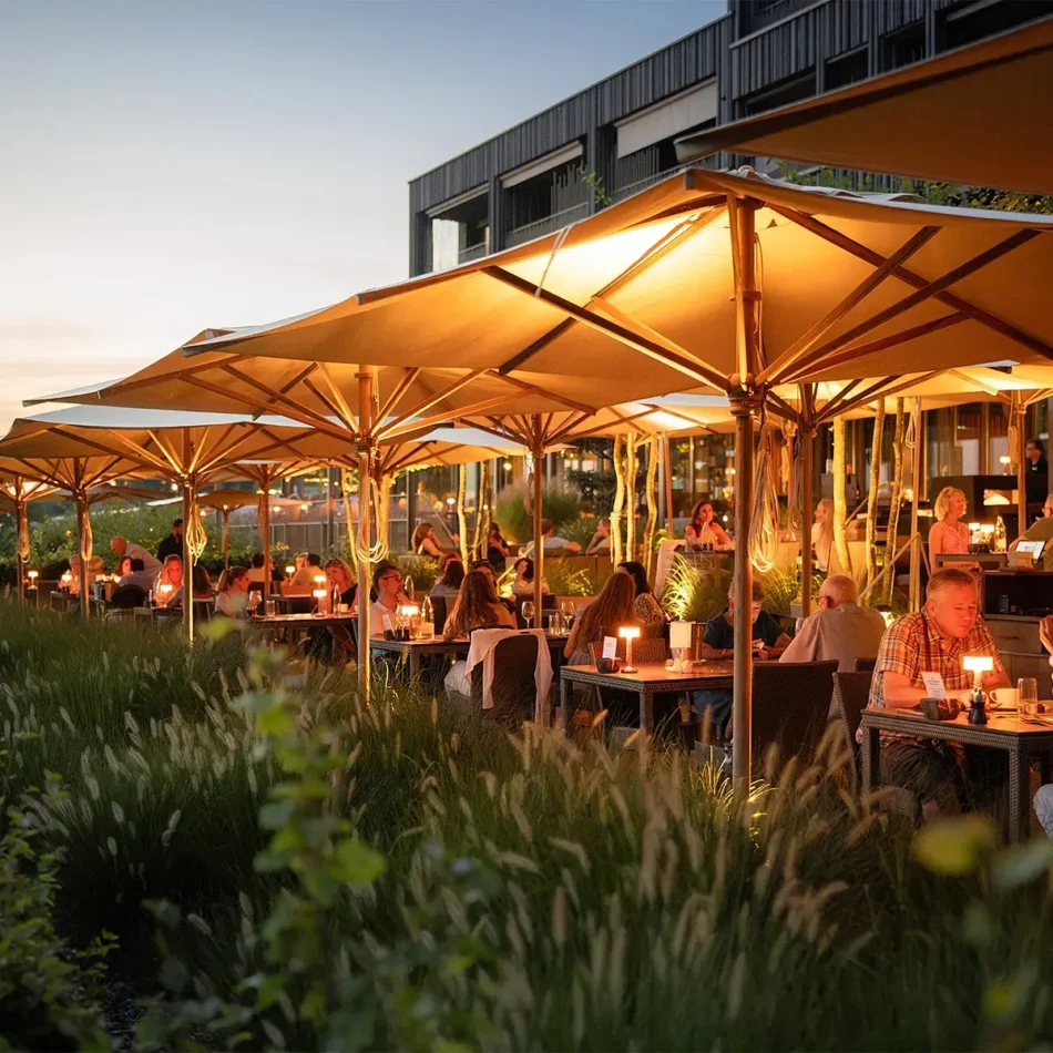 Terrasse des Sonne Seehotels Eich: Gäste in der Abenddämmerung unter warm beleuchteten Sonnenschirmen