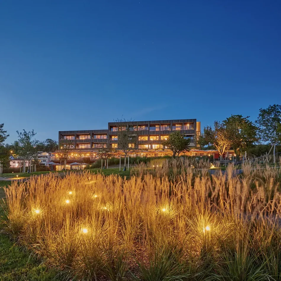 Blaue Stunde am Sonne Seehotel: warm beleuchtete Fassade, davor angestrahlte Gräser im Garten